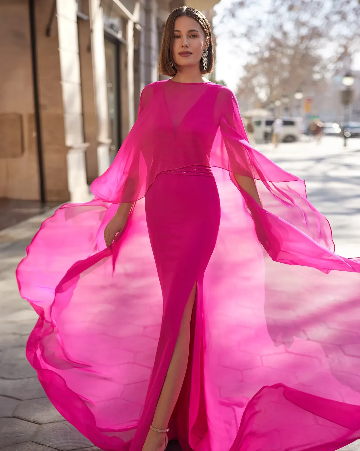 Una mujer lleva un vestido largo rosa con mangas largas y una abertura alta.