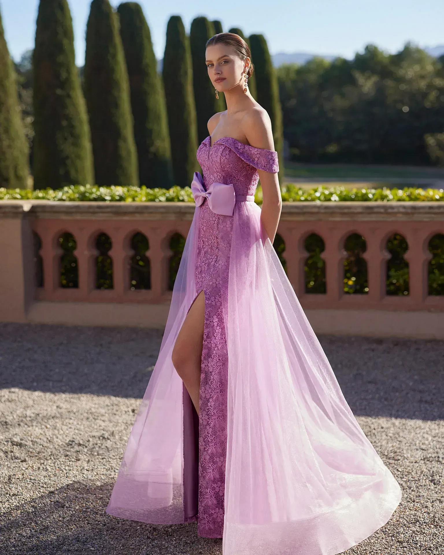 Una mujer con un vestido morado está parada frente a una valla.