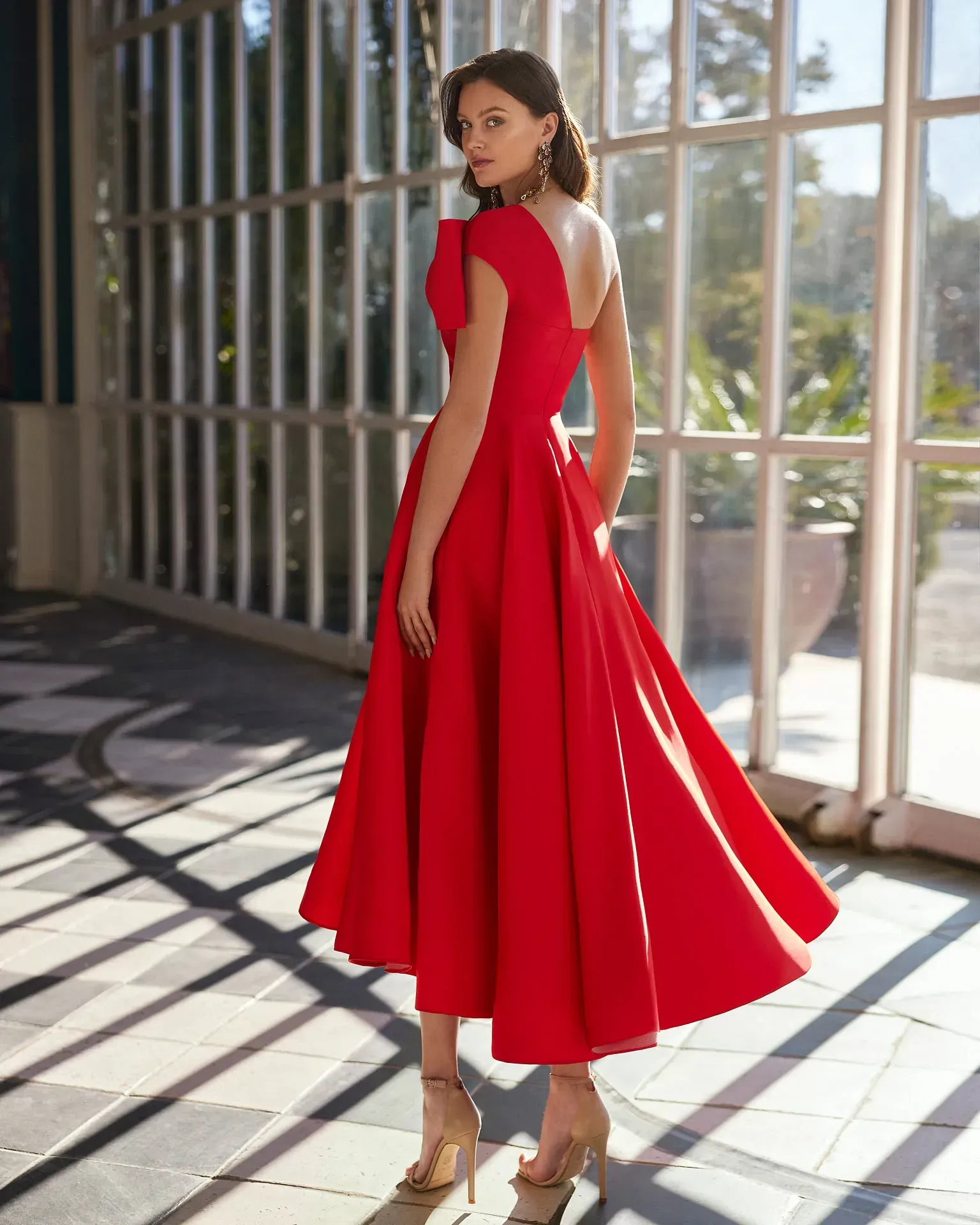 Una mujer con un vestido rojo está parada frente a una ventana.