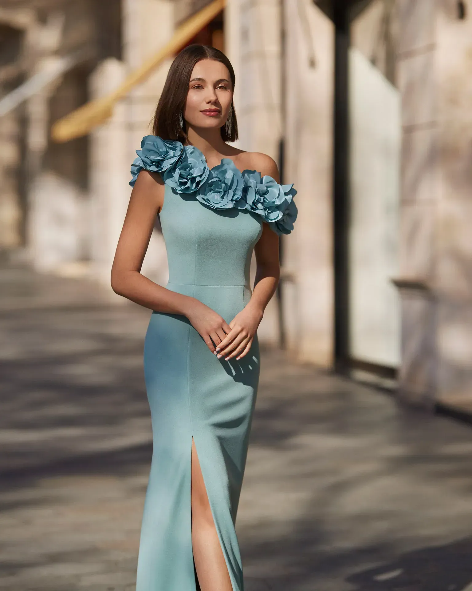 Una mujer con un vestido azul con volantes en los hombros está parada en una acera.