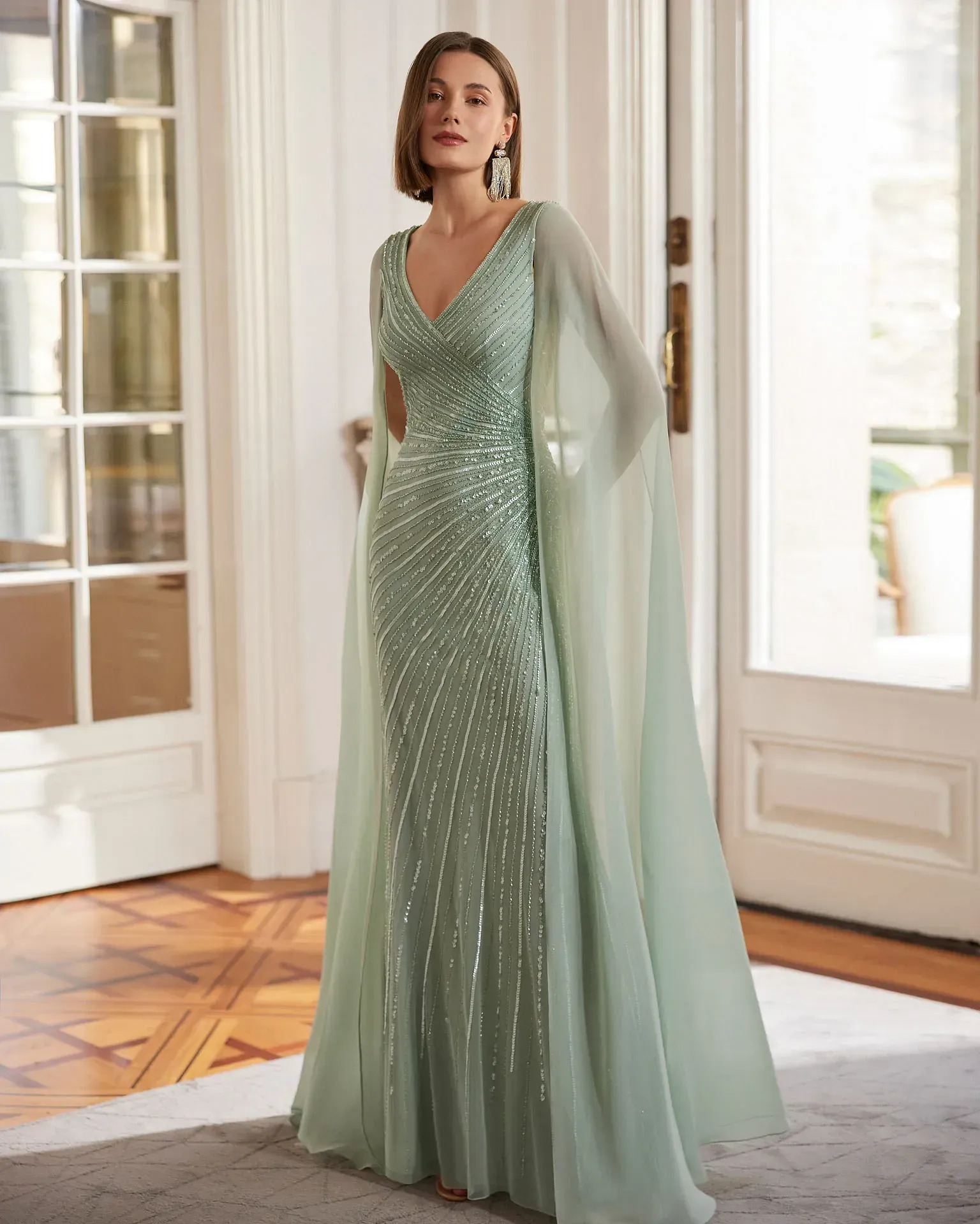 Una mujer lleva un vestido largo verde con una capa.