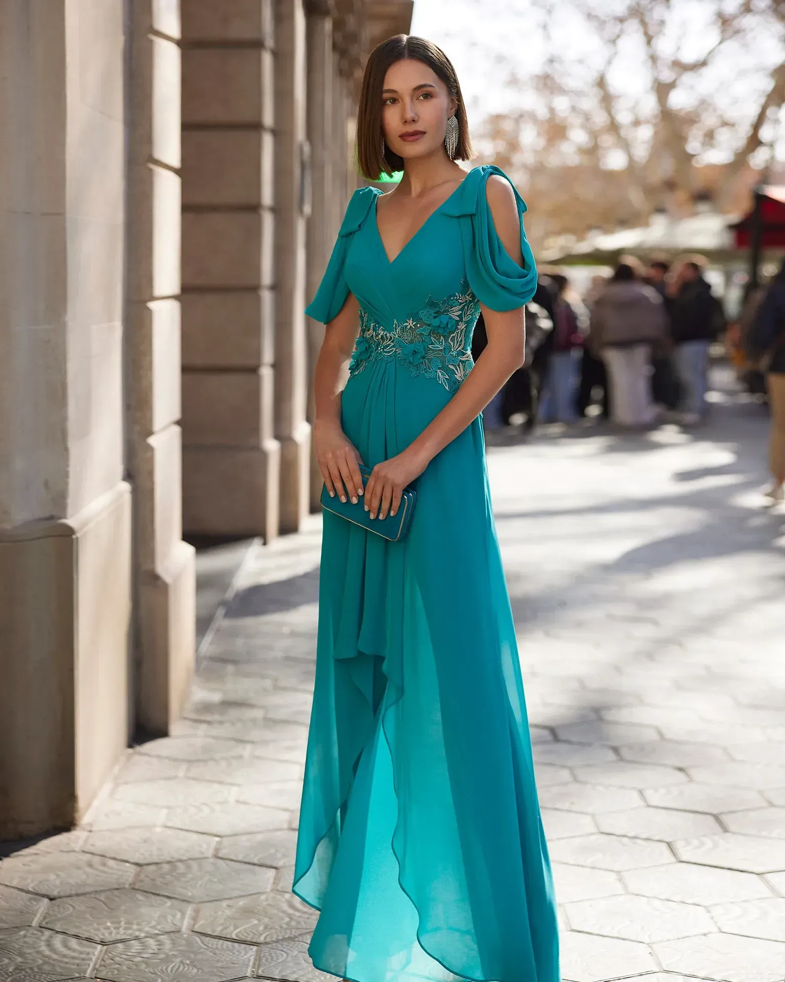 Una mujer con un vestido largo verde está parada en una acera.
