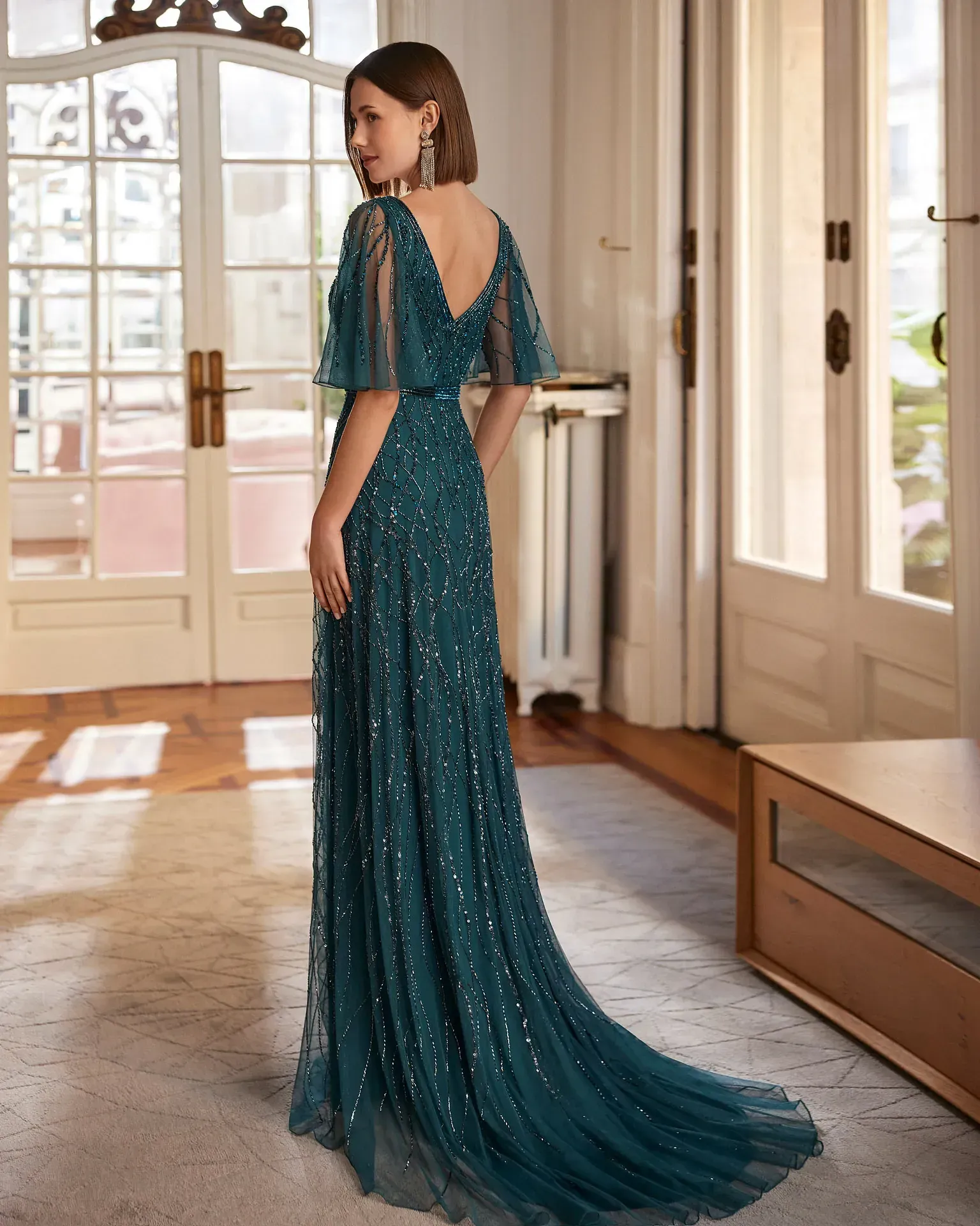 Una mujer con un vestido largo azul está parada en una sala de estar.