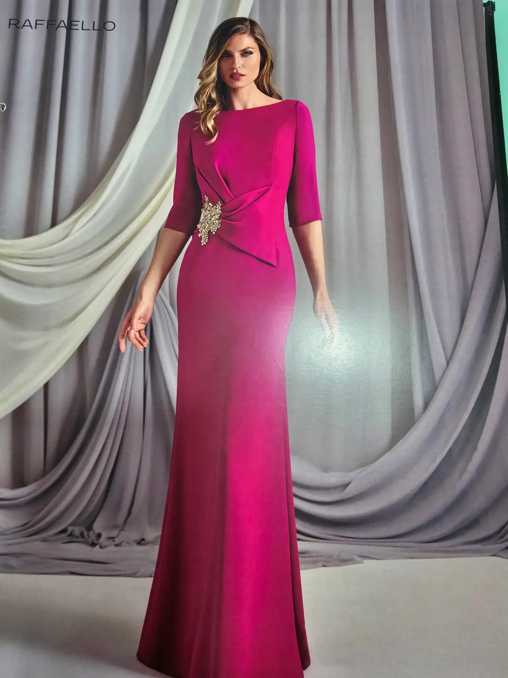 Una mujer con un vestido largo de color rosa está parada frente a una cortina gris.