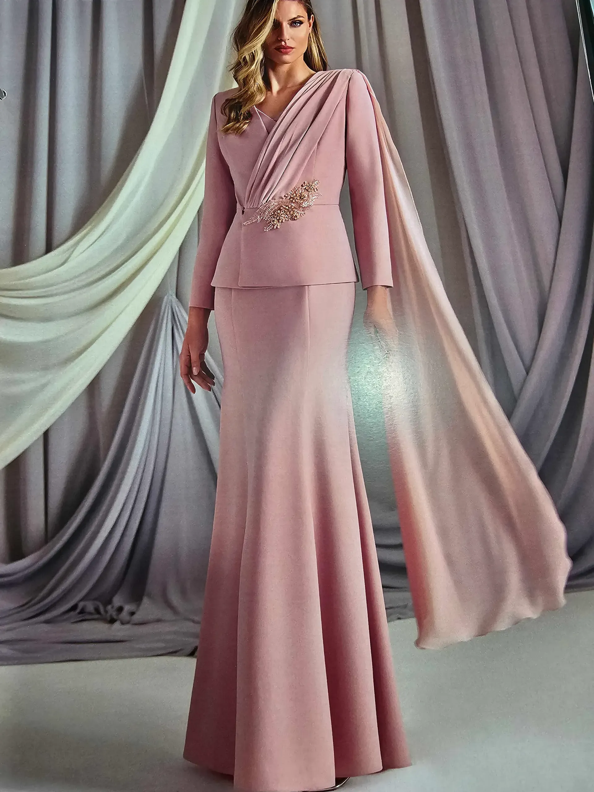Una mujer lleva un vestido largo rosa con una capa.