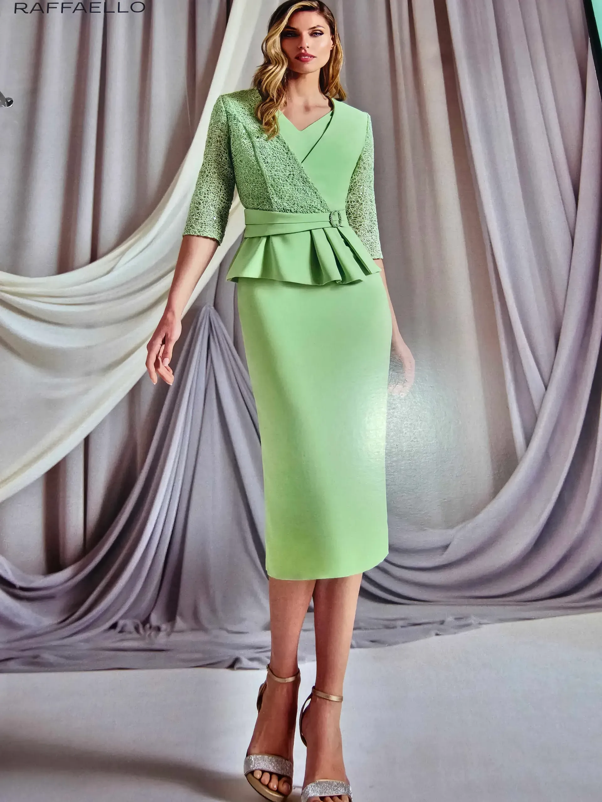 Una mujer con un vestido verde está parada frente a una cortina.