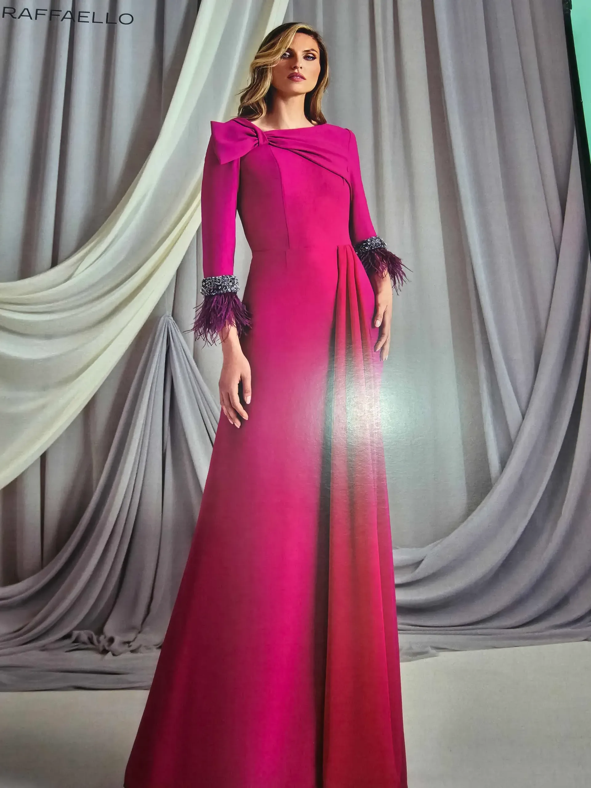 Una mujer lleva un vestido largo rosa con plumas en las mangas.