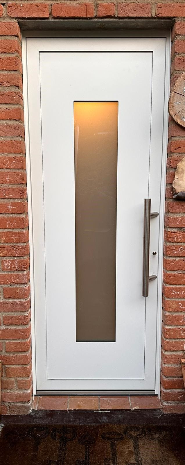 An einer Backsteinmauer befindet sich eine weiße Tür mit einem Glasfenster.