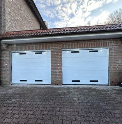 An einem Backsteingebäude befinden sich zwei weiße Garagentore.
