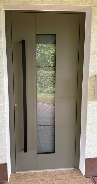 Eine graue Tür mit einem schwarzen Griff und einem Glasfenster.