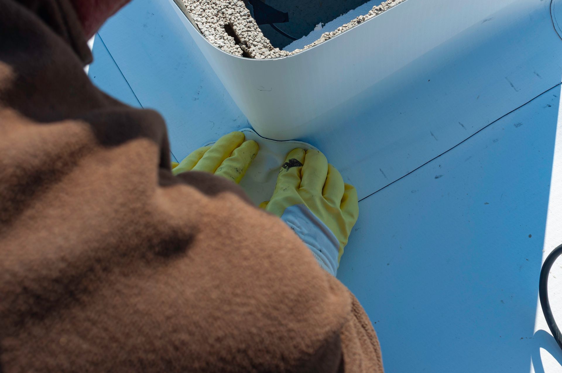 Une personne portant des gants de protection jaunes utilise un poste de soudage thermique pour sceller une membrane de toiture blanche autour de la base d'une cheminée.