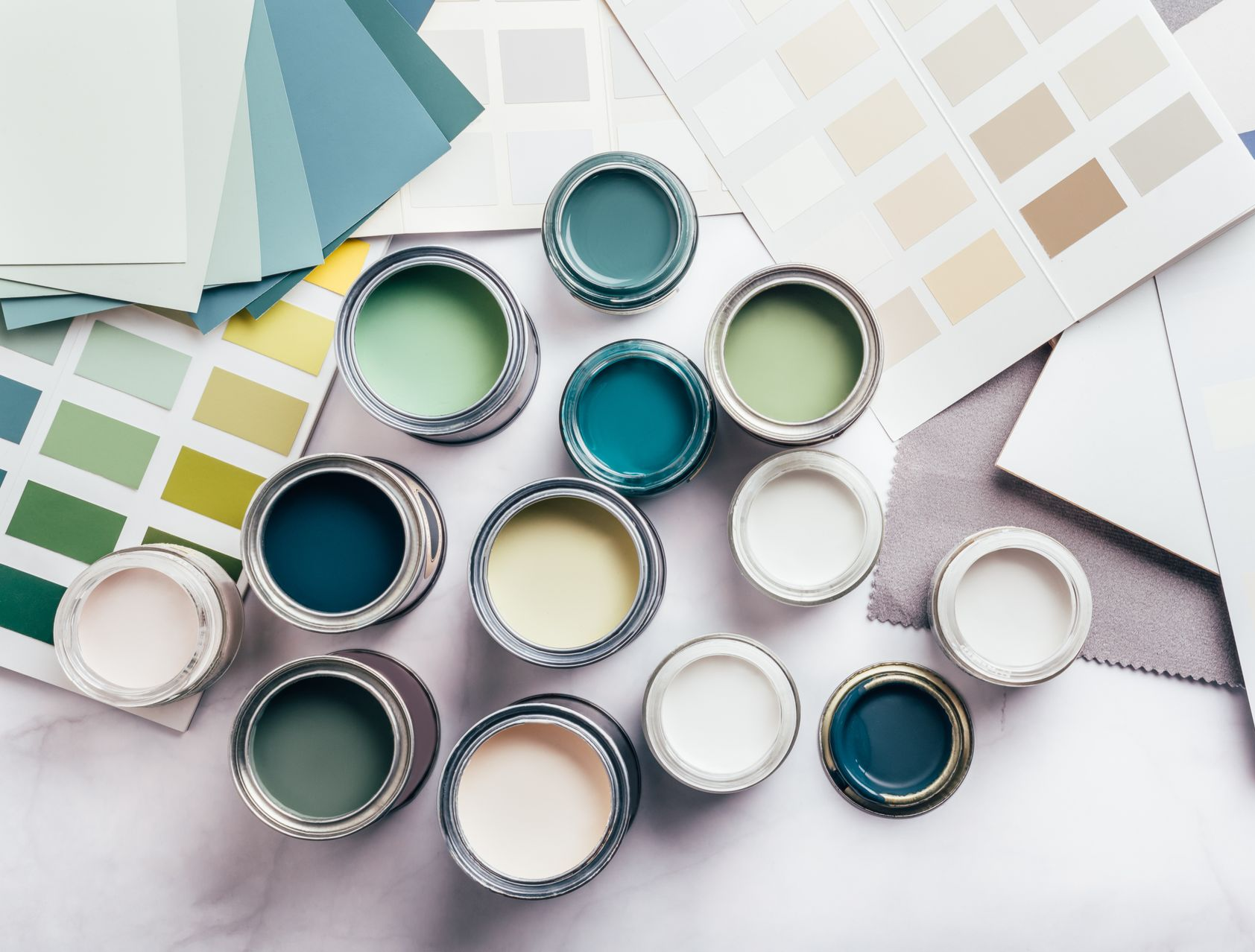 Un assortiment de pots de peinture aux nuances de vert, de bleu et de blanc est disposé à côté de plusieurs palettes de couleurs sur une surface.