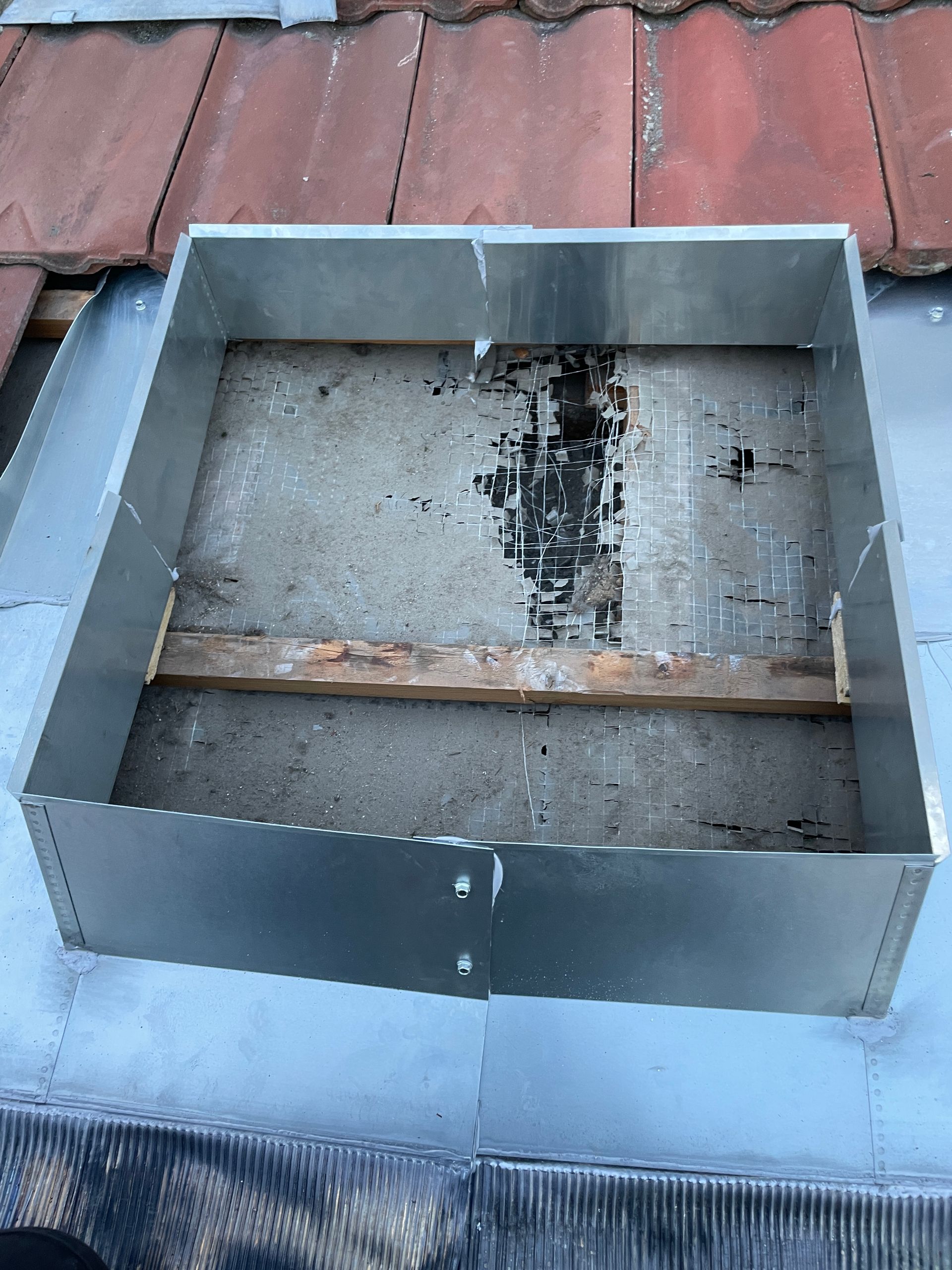 Une personne vêtue de sombre installe un matériau de toiture noir sur le toit plat d'un bâtiment situé à côté d'une zone de gravier.