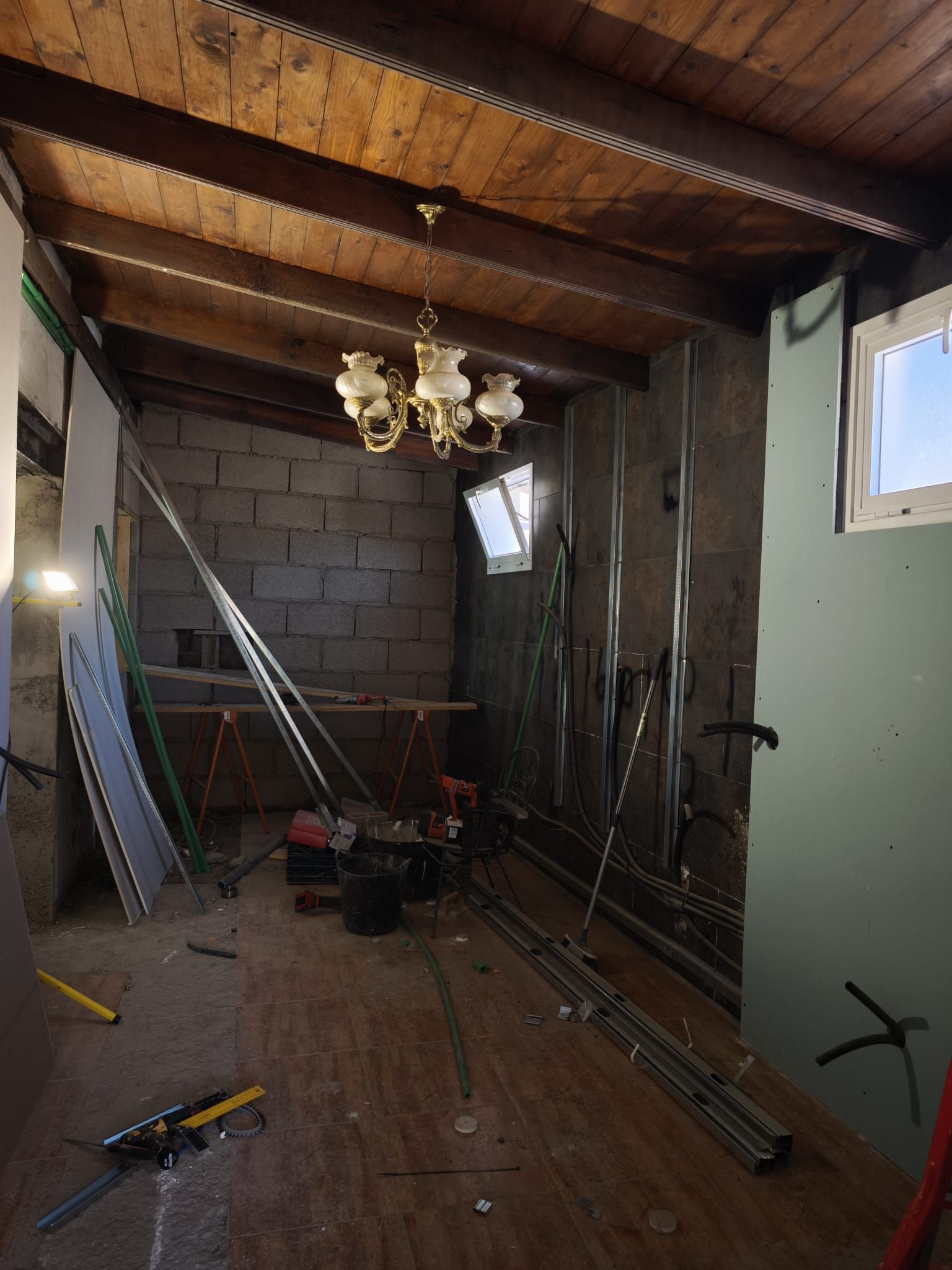 Obra de renovación con una escalera, herramientas, vigas a la vista y una lámpara de araña en una habitación sin terminar