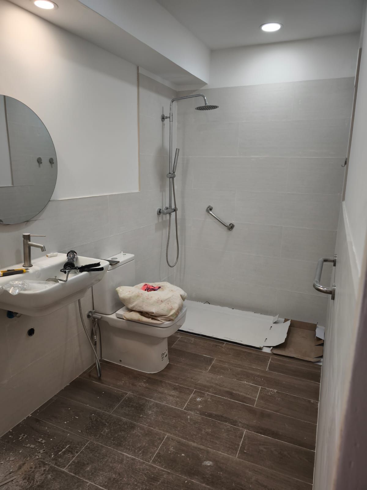 Baño accesible con lavabo, inodoro, ducha y barra de apoyo en el suelo de baldosas marrones