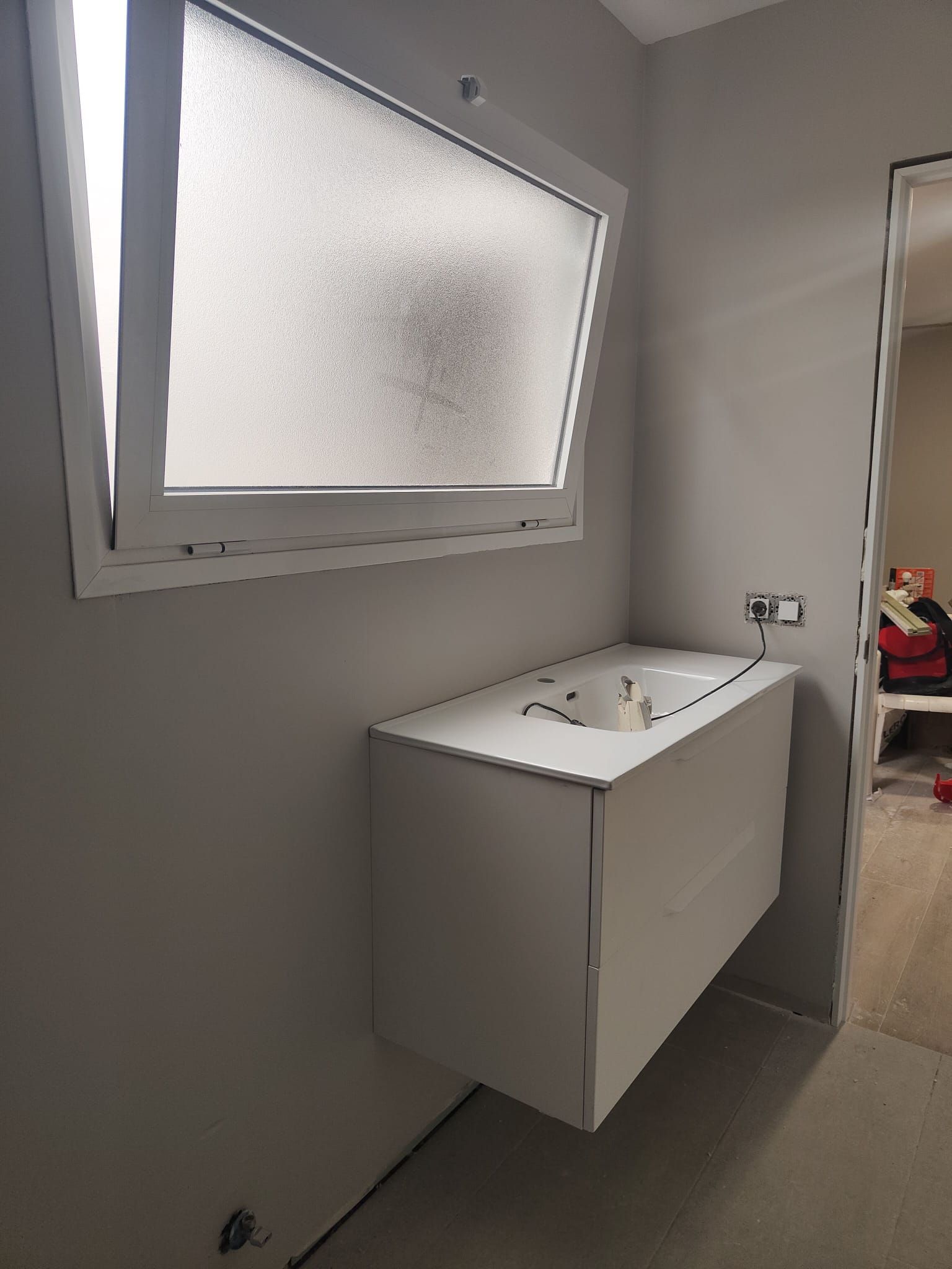 Baño pequeño con paredes grises, ventana esmerilada y lavabo blanco de pared.