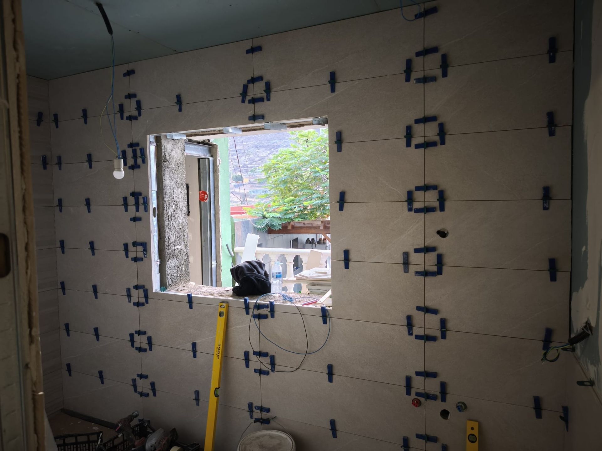Pared interior en construcción con paneles aislantes, un hueco para una ventana y una escalera amarilla apoyada contra la pared.