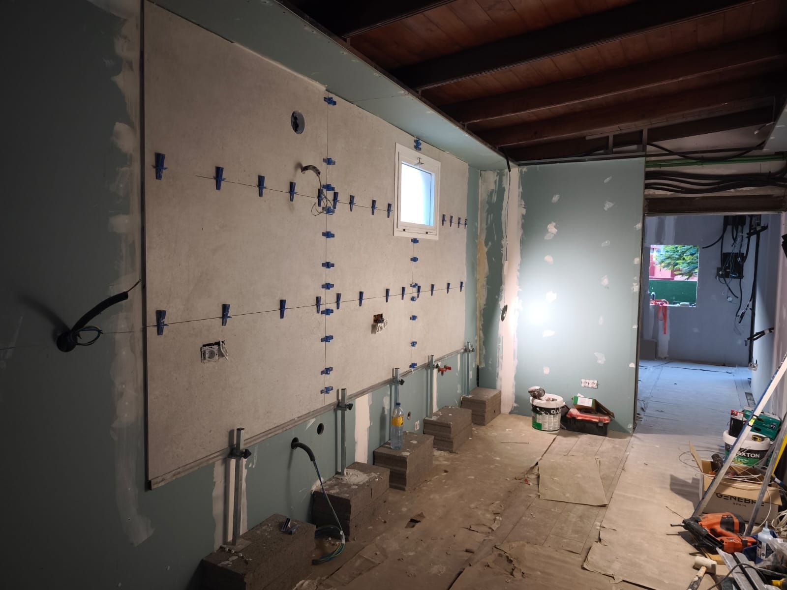 Habitación sin terminar, con paneles de yeso, vigas del techo a la vista y herramientas de construcción esparcidas por el suelo.