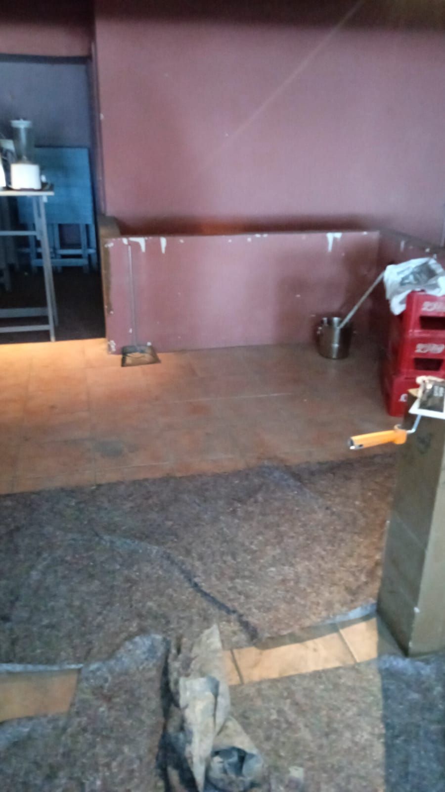 Habitación vacía con una pared marrón, suelo enmoquetado, una mesita, una silla y un electrodoméstico rojo a la derecha.