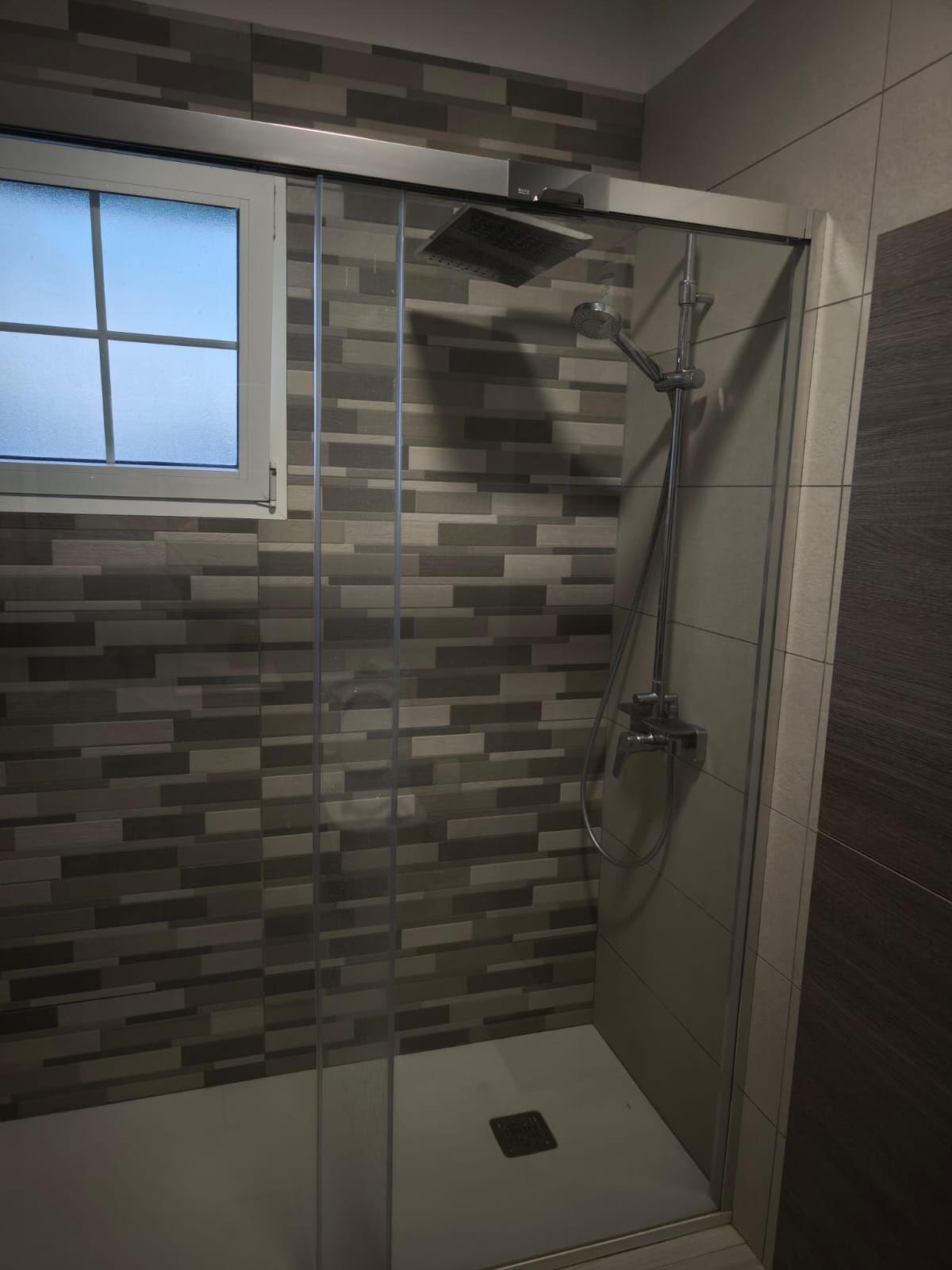 Ducha de baño moderna con azulejos, mampara de vidrio, cabezal de ducha tipo lluvia y desagüe cuadrado en el suelo