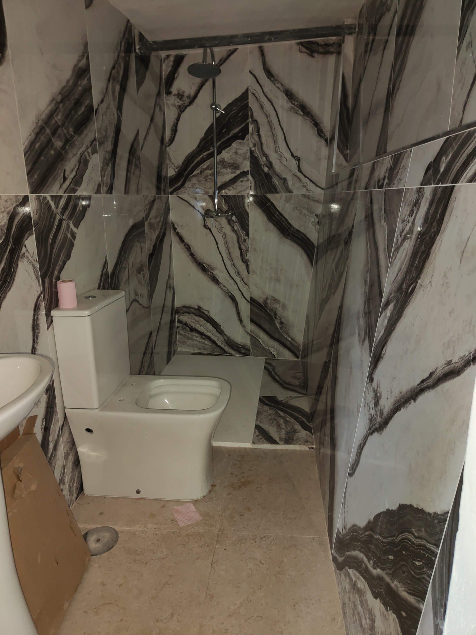 Baño pequeño con un inodoro y un lavabo blancos, azulejos de pared con efecto mármol en blanco y negro y suelo beige.