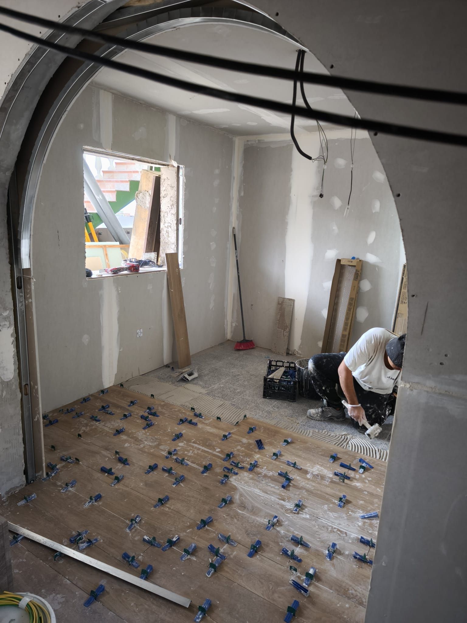 Habitación parcialmente renovada, con el techo a la vista, el suelo sin terminar y un trabajador agachado junto a unas herramientas.