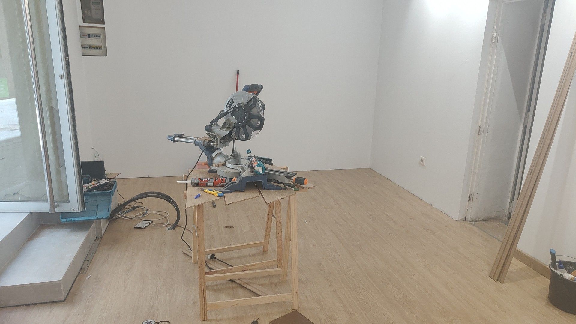 Pequeño robot en un carrito de madera en una habitación con pocos muebles, paredes blancas y suelo de madera clara.