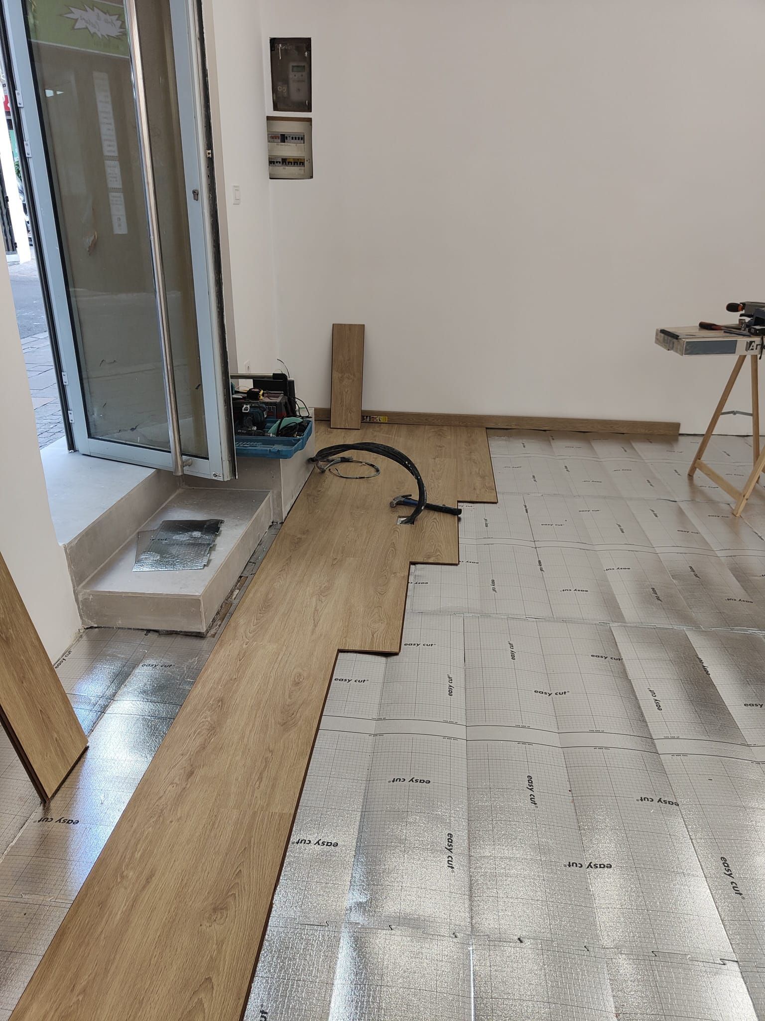 Habitación interior con el suelo nuevo parcialmente instalado junto a una puerta abierta.