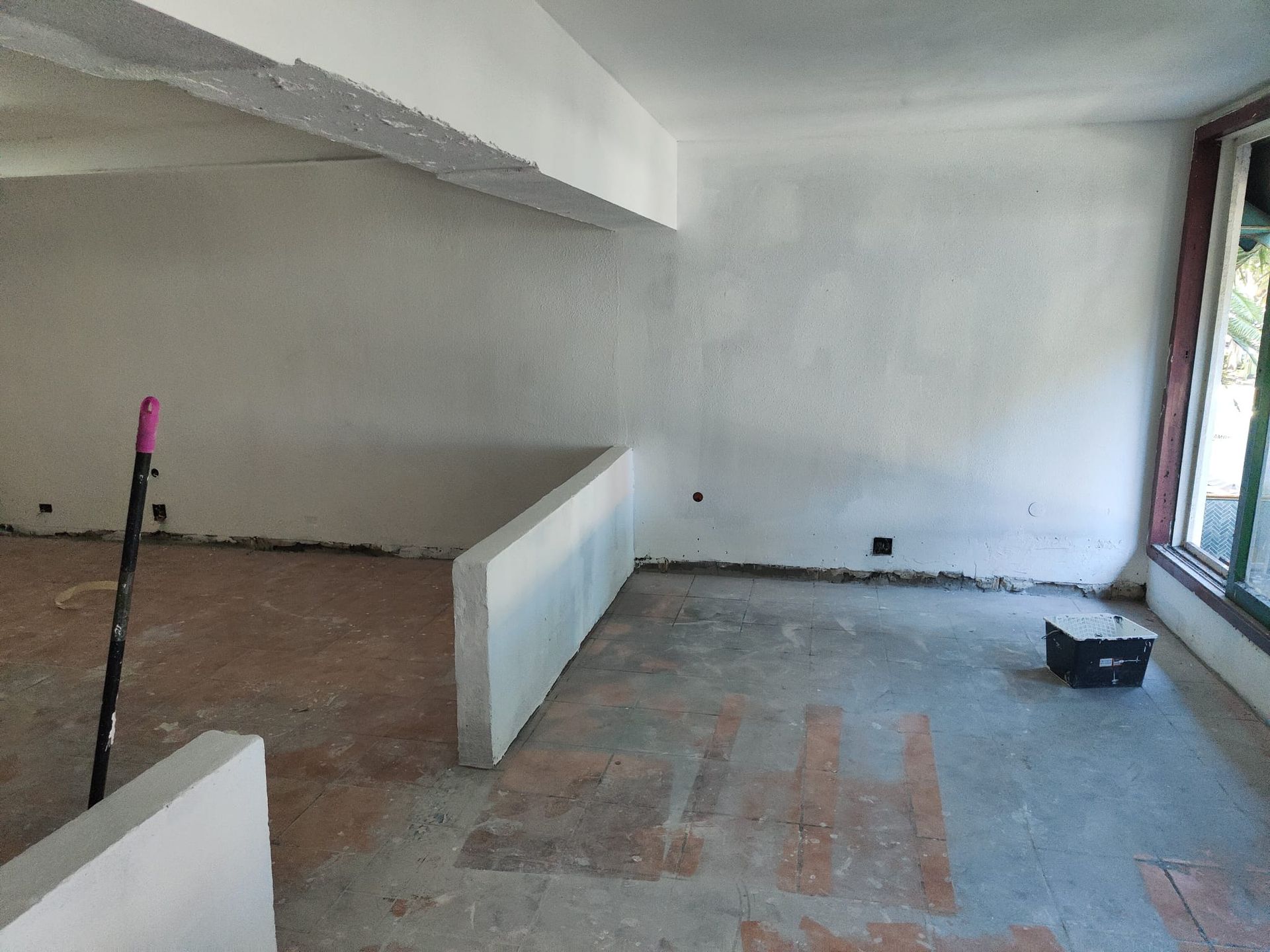 Habitación vacía y sin terminar, con paredes blancas, suelo al descubierto y una ventana grande a la derecha.
