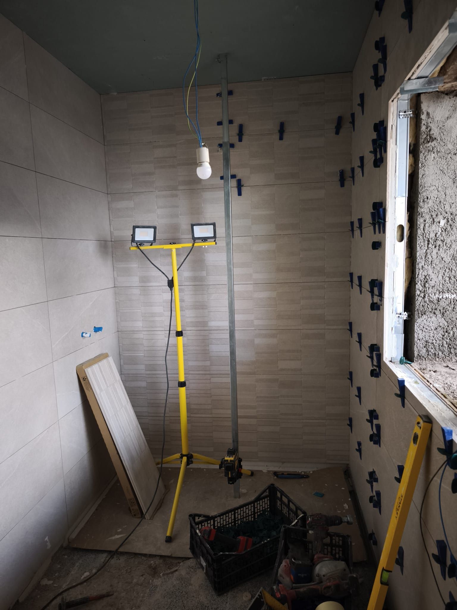 Baño parcialmente alicatado en obras, con luz de trabajo amarilla, herramientas y escombros en el suelo
