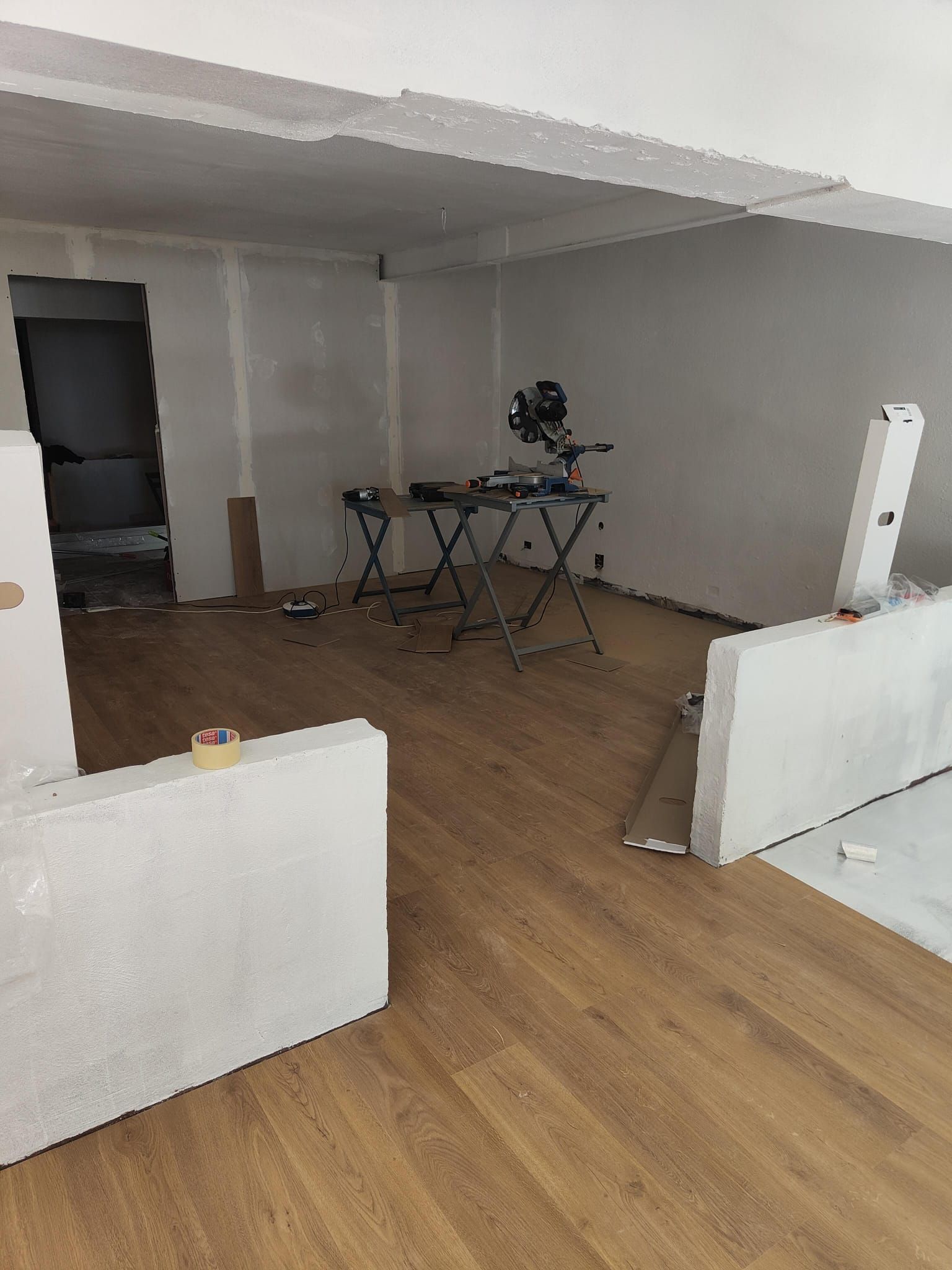 Habitación vacía con suelo de madera, una mesa plegable y paredes divisorias blancas en remodelación.
