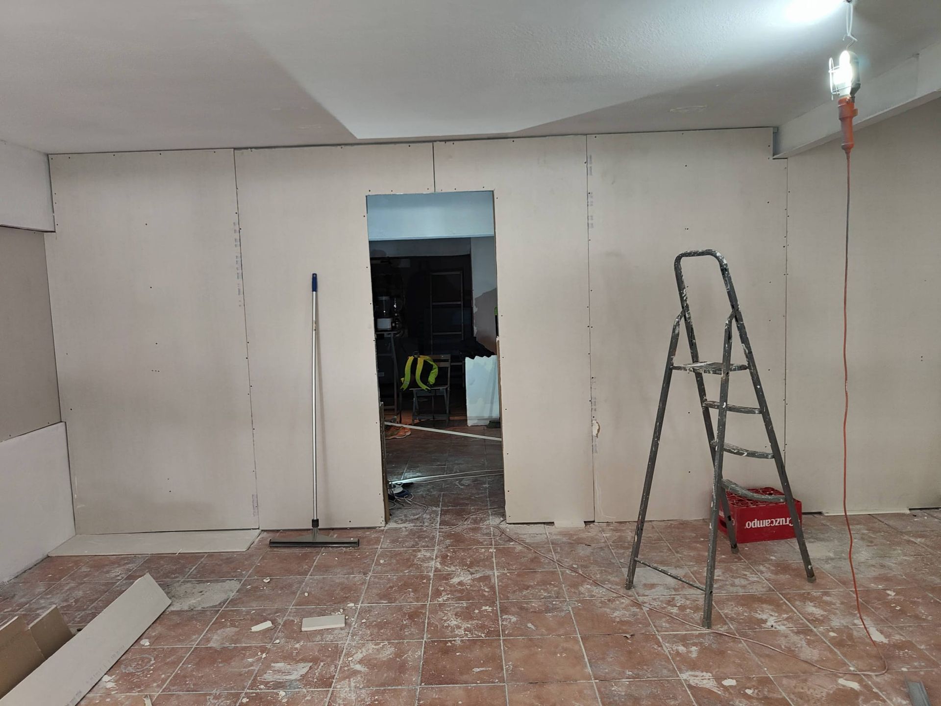 Habitación parcialmente renovada, con paredes de pladur blancas, una puerta abierta, una escalera y escombros de obra en el suelo