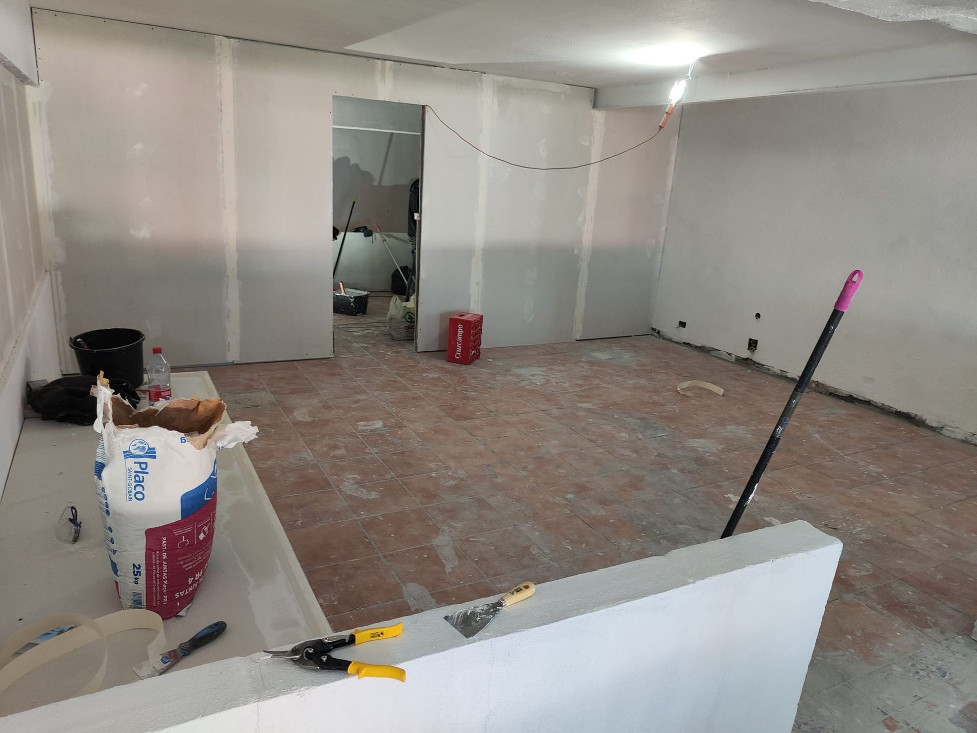 Habitación sin terminar, con paredes blancas, suelo al descubierto, herramientas y materiales de construcción esparcidos por todas partes.