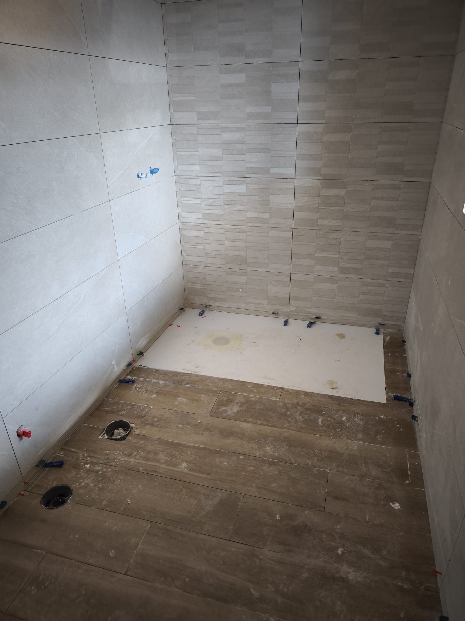 Baño parcialmente alicatado, con paredes sin terminar y desagües del suelo a la vista