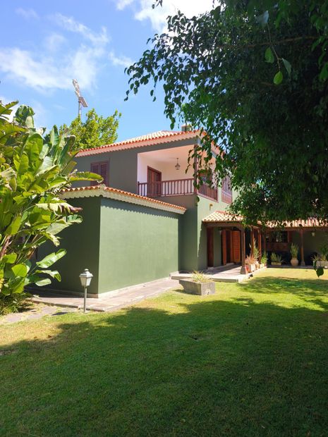 Casa rosa de dos pisos con una pared verde y un exuberante jardín bajo un cielo azul brillante