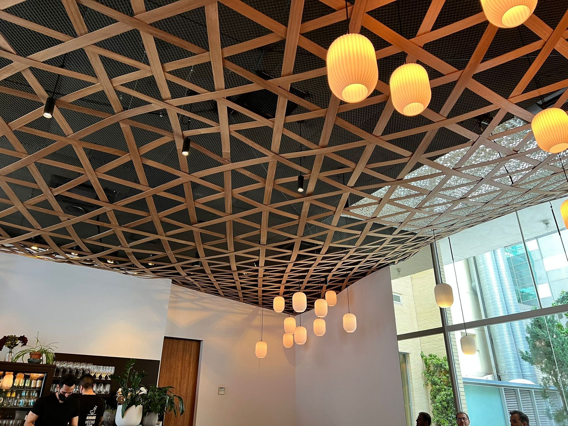 Interior de una cafetería moderna con techo geométrico de madera y faroles colgantes
