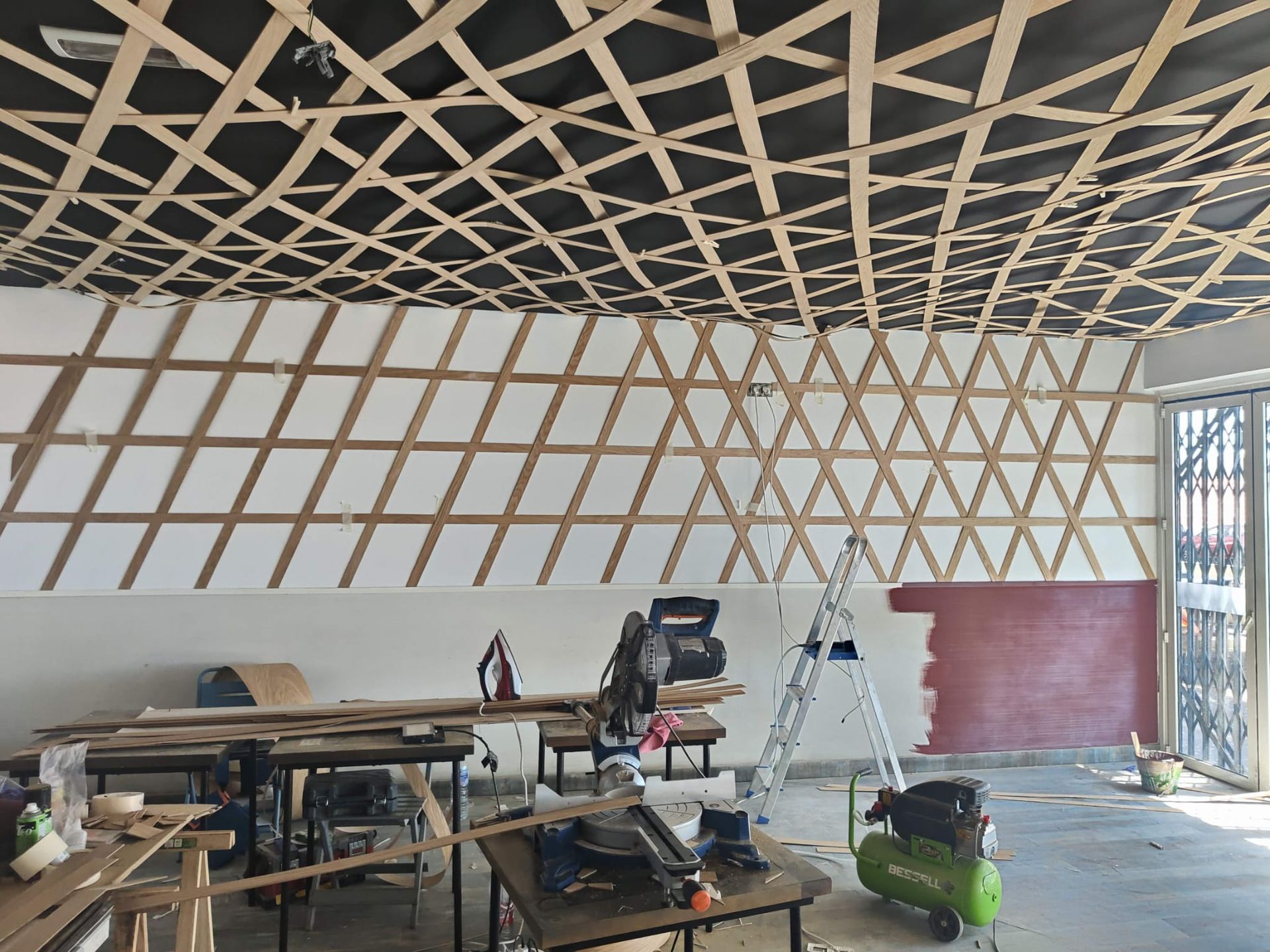 Obra interior con techo de celosía a la vista, escaleras, herramientas y paredes sin terminar