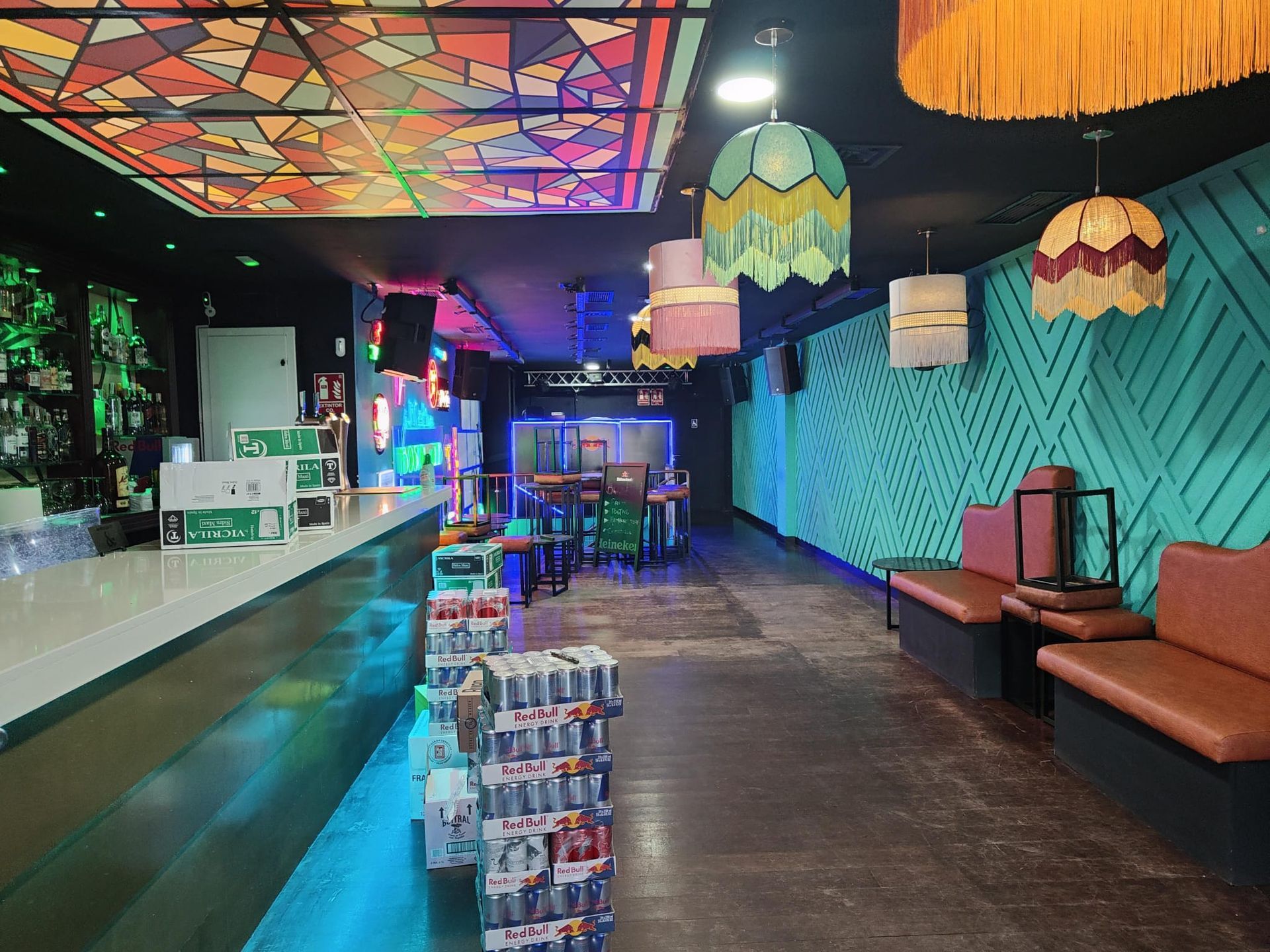 Interior colorido de un bar retro, con techo estampado, pared turquesa, reservados y estanterías con bebidas