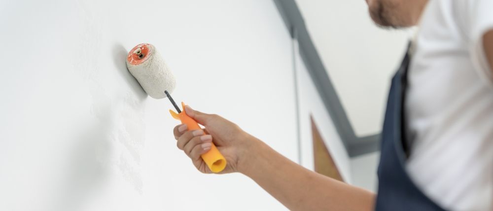 Persona pintando una pared blanca con un rodillo de mango amarillo