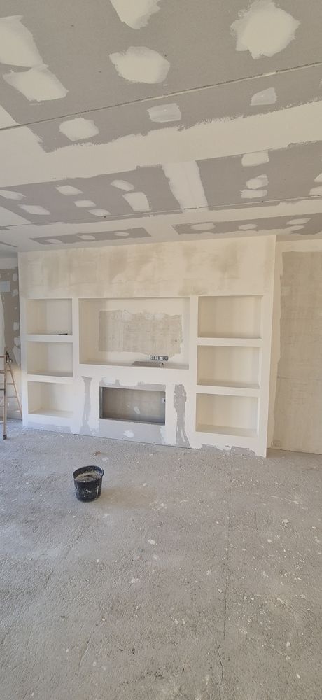 Habitación parcialmente terminada, con paneles de yeso, estanterías empotradas y una chimenea en construcción