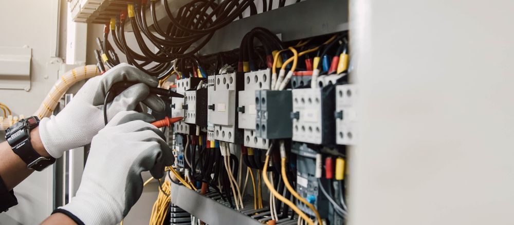 Técnico con guantes cableando un cuadro de control eléctrico con cables de colores y disyuntores