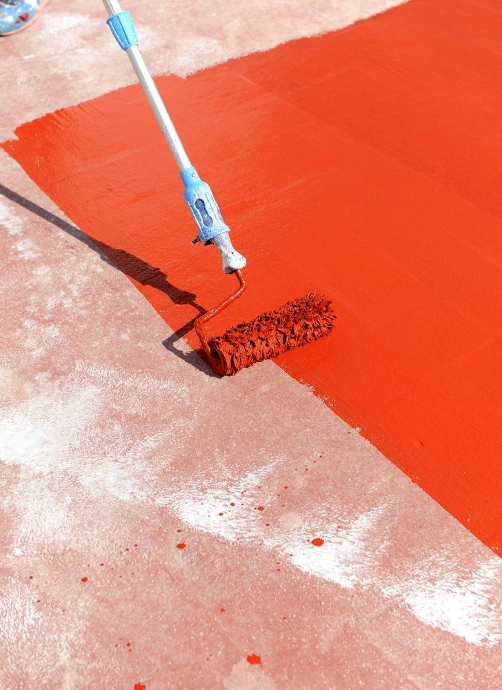 Pintando un suelo de hormigón de color rojo vivo con un rodillo y un mango extensible