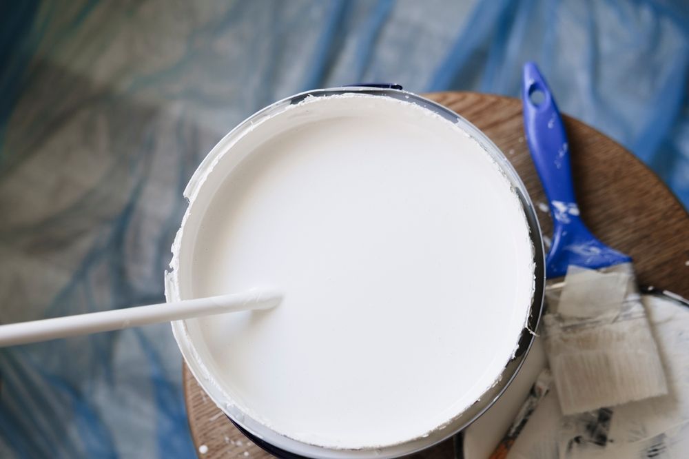 Abre una lata de pintura blanca y coloca unos pinceles sobre una superficie de madera