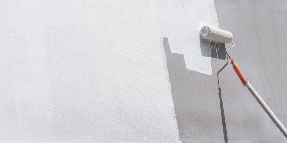 Rodillo aplicando pintura blanca a una pared cerca de una esquina, con una extensión de mango rojo.