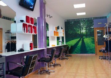 Interior de salón moderno con sillones de peluquería, espejos, estantes y un mural de un bosque en la pared del fondo.