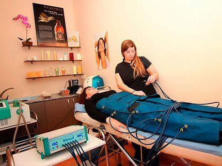 Una persona recibe un tratamiento de spa en una camilla de masaje mientras un técnico opera el equipo en una sala de bienestar.