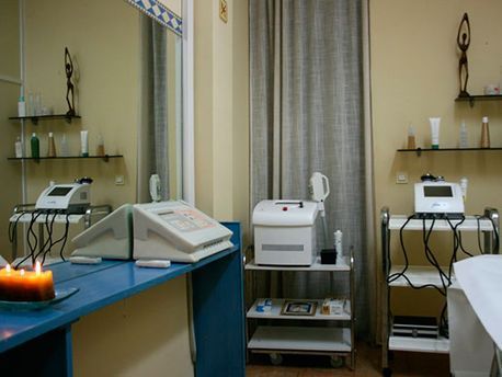 Sala de tratamiento estéril con camilla azul, instrumental médico, estanterías y ventana con cortinas.