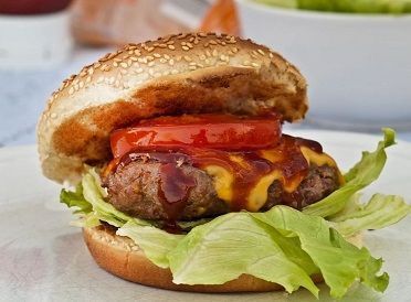 Una hamburguesa con queso, lechuga, tomate y salsa barbacoa en un pan de sésamo tostado, servida en un plato blanco.