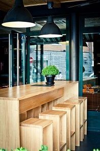 Una barra alta de madera con taburetes a juego, una pequeña planta en maceta y lámparas colgantes negras.