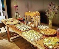 Una mesa tipo bufé dispuesta con una variedad de aperitivos, bocadillos y pequeños postres, decorada con un jarrón de flores.